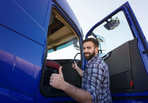 Professional truck driver entering his truck long vehicle and holding thumbs up.